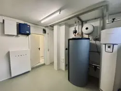 Moderner Heizungsraum mit Wärmepumpe, Warmwasserspeicher und technischer Gebäudeausstattung.