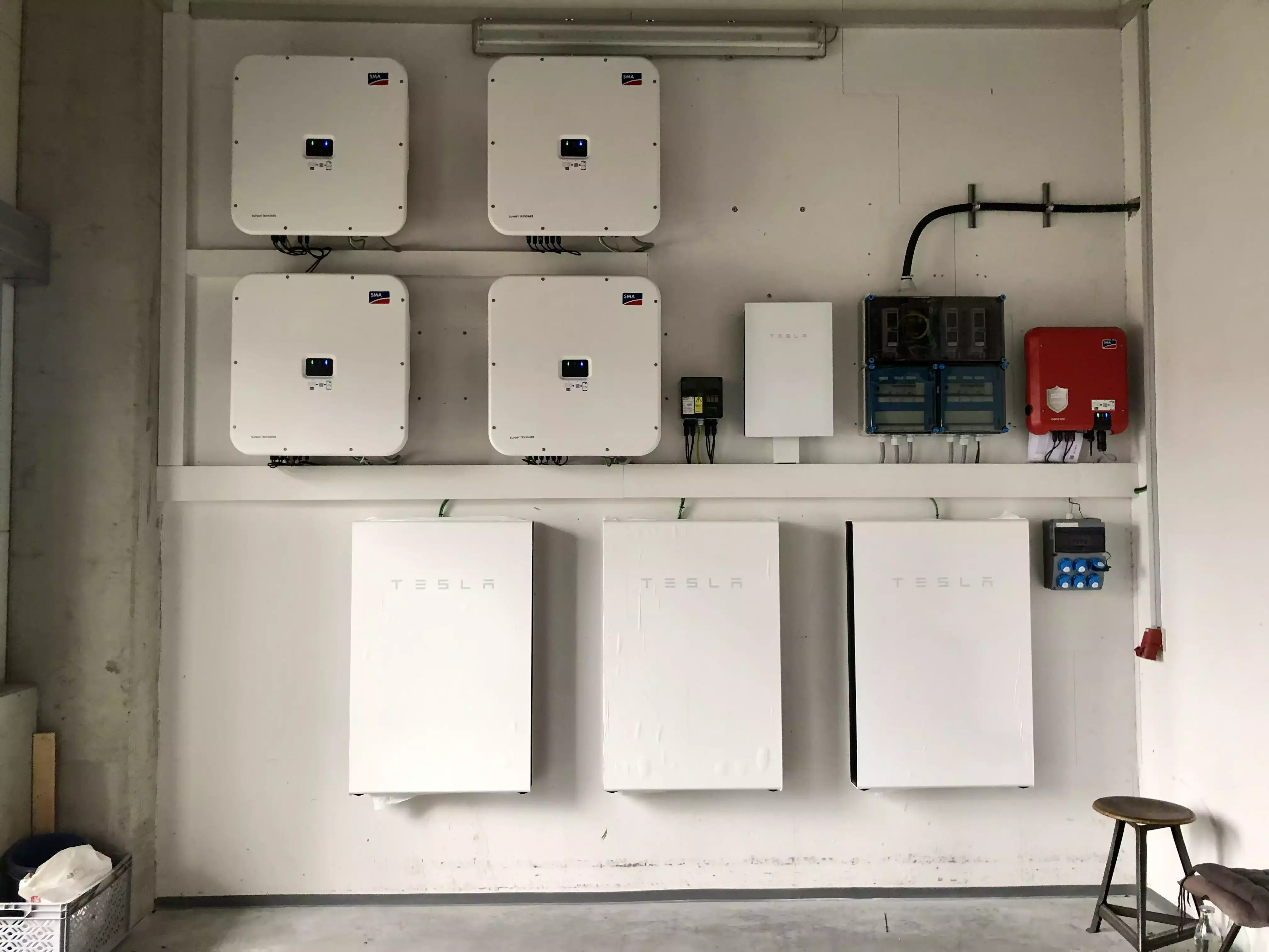 Mehrere Tesla Powerwall Stromspeicher und Wechselrichter sind an einer Wand in einem Technikraum installiert.