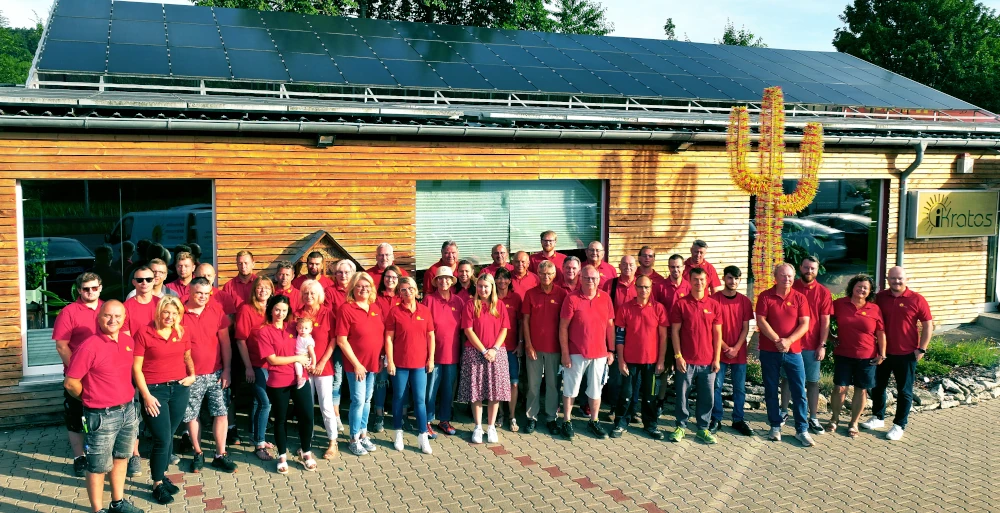 Eine große Gruppe Menschen in roten Shirts steht vor einem Gebäude mit Solaranlage und Holzfassade.